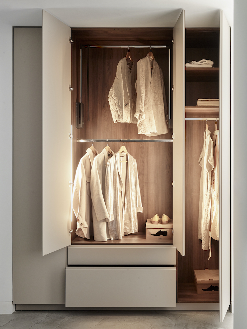 Bespoke wardrobe interior with illuminated walnut hanging rails, double-height clothing storage, integrated LED lighting, pale grey lacquered exterior doors and soft-close drawer units