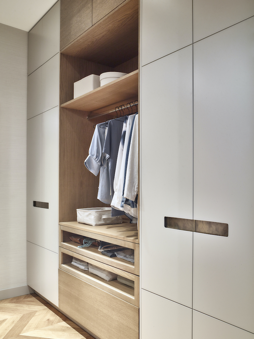 Minimalist bespoke wardrobe with pale oak interior framework, matte grey lacquered doors, bronze metal handles, integrated hanging rail, pull-out shoe storage drawers, and natural light wood flooring