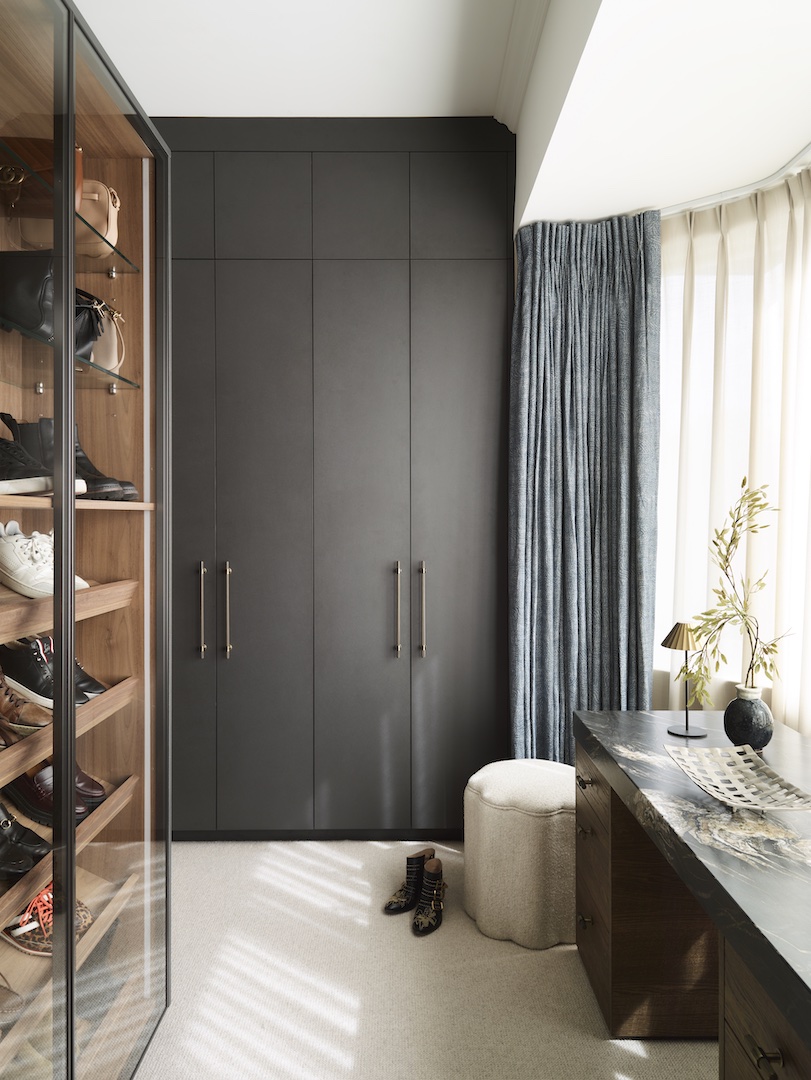 Custom fitted wardrobe with stone grey lacquered doors and copper bar handles revealing oak interior with LED shelf lighting, hanging rail, and organized storage compartments on grey stone flooring