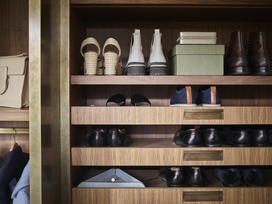 Bespoke walnut shoe storage system with integrated pull-out drawers, organised display shelving for dress shoes, boots, and accessories including sage green hat boxes and leather goods