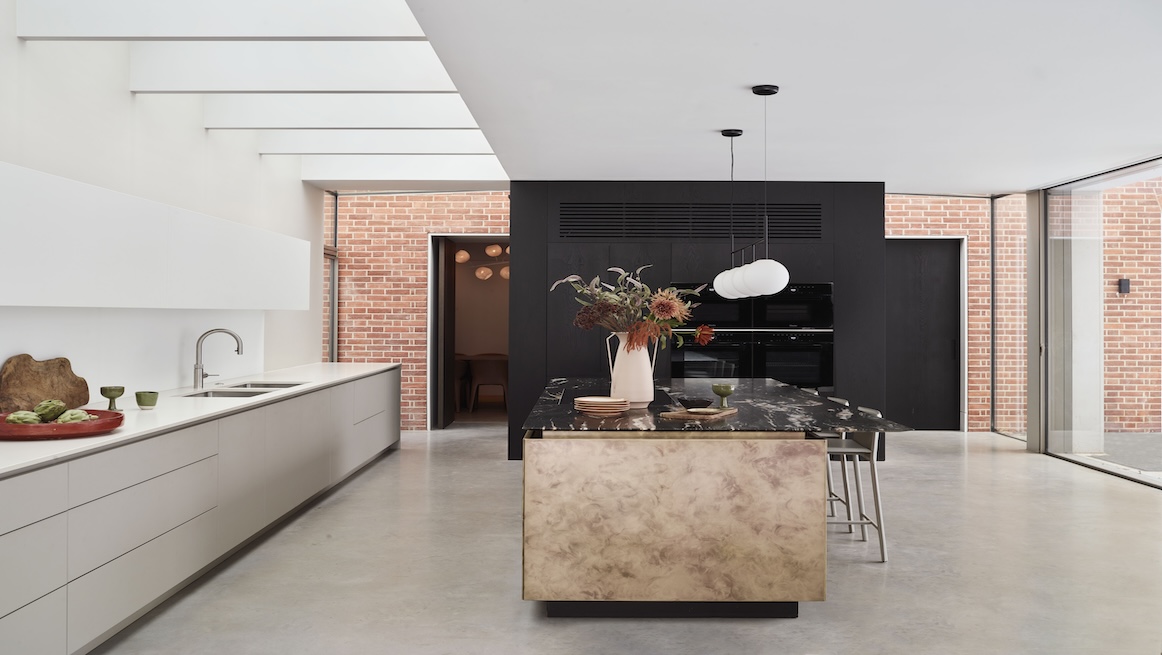 Elegant kitchen design with a blend of classic and modern details. Features a marble island with brass fixtures, wood panel cabinetry, decorative ceiling mouldings, and integrated ovens within tall storage units.