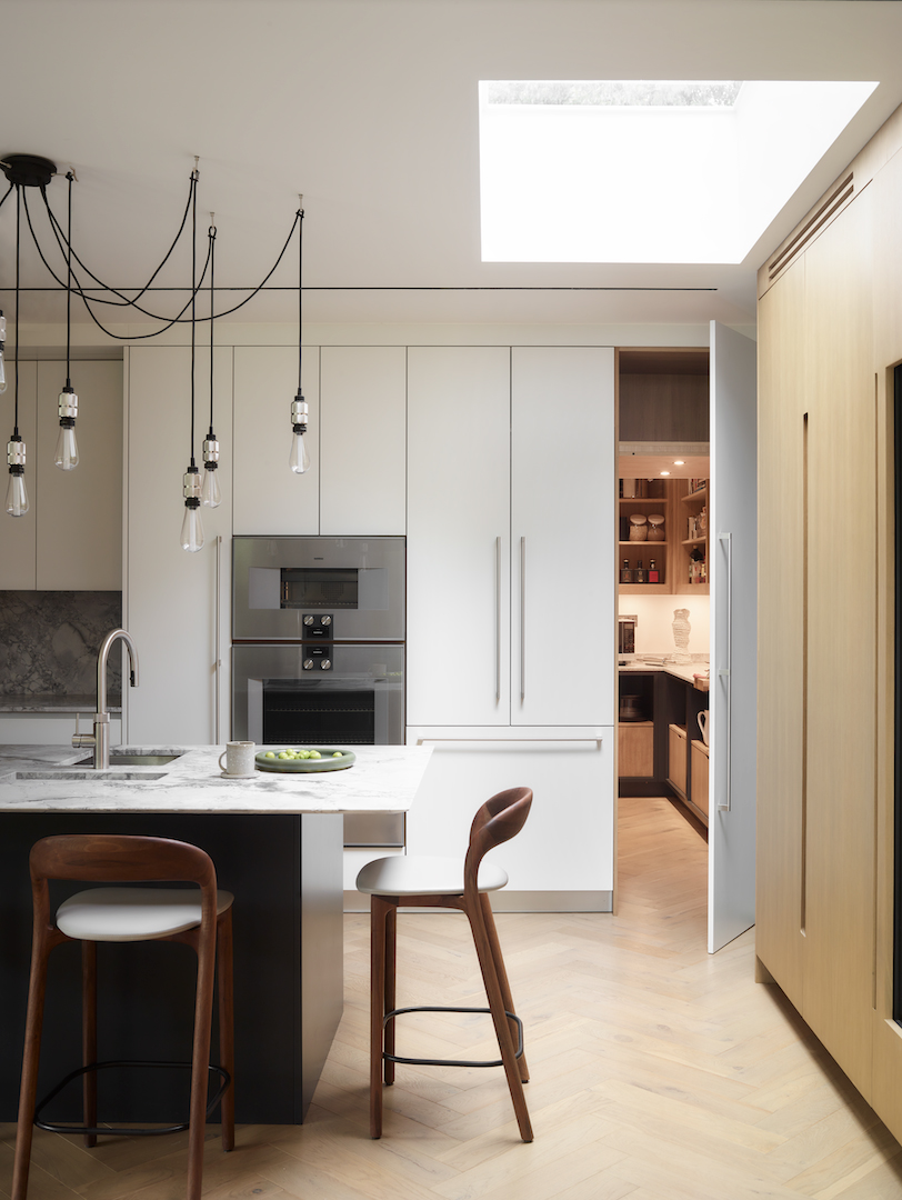 Contemporary open-plan kitchen with dark cabinetry, black stone island, and wine storage. Includes integrated appliances, a mix of open shelving and concealed storage, plus modern lighting for a sleek luxury finish.
