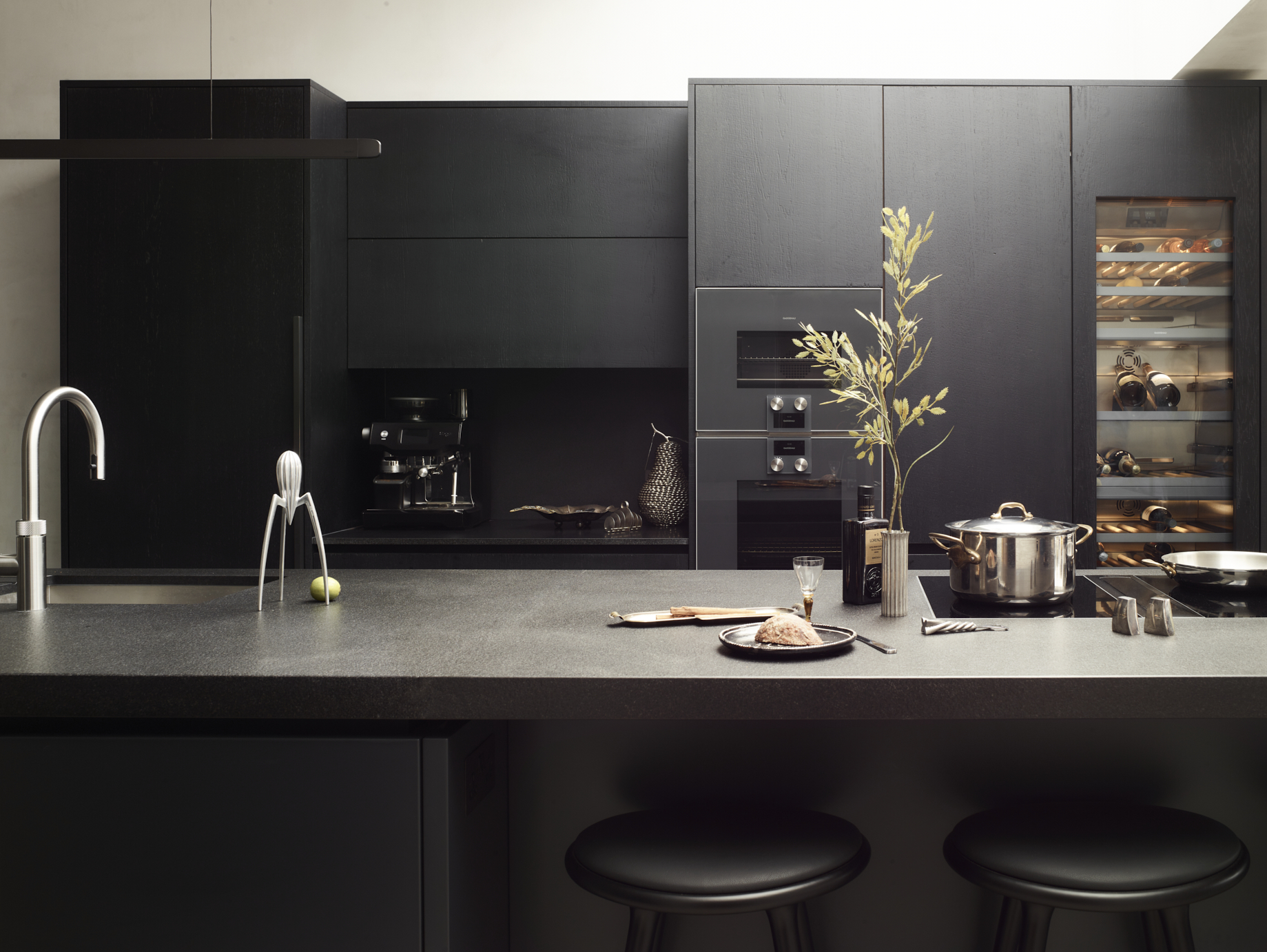 Contemporary dark kitchen featuring "Let's talk" invitation with built-in wine storage, stainless steel cookware, white tap, and "BOOK A DESIGN MEETING" call-to-action, emphasising collaborative approach to bespoke kitchen design