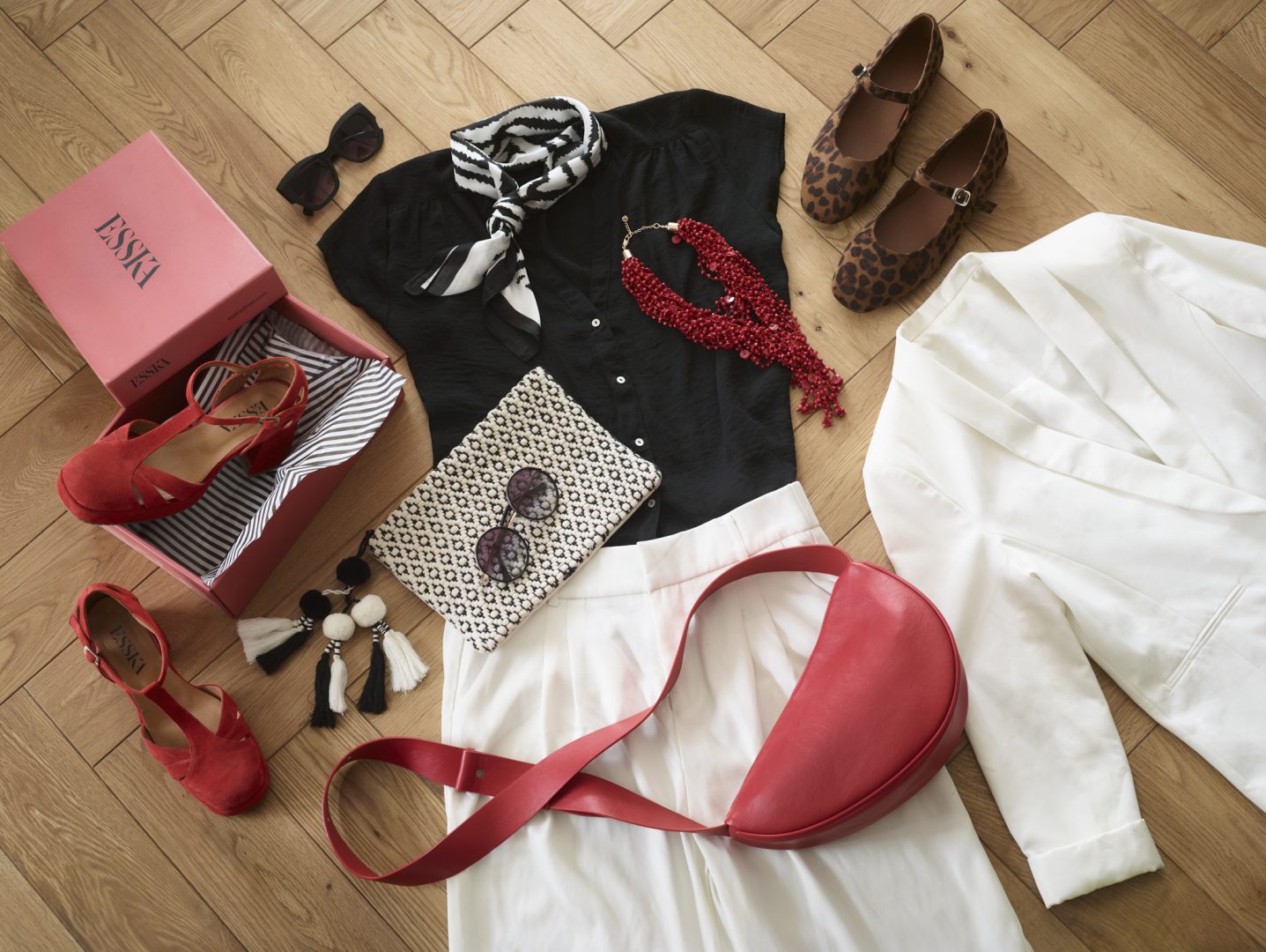 Fashion flatlay on herringbone parquet flooring featuring black cardigan, leopard print shoes, red handbag, patterned scarf, jewellery, and shopping bags creating lifestyle styling composition unrelated to kitchen design