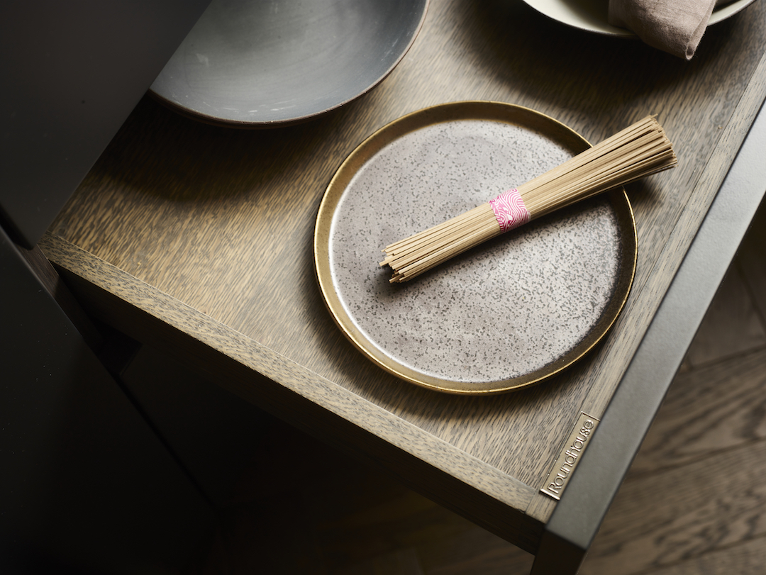 Roundhouse drawer detail showcasing oak grain texture with speckled ceramic plate, bamboo chopsticks wrapped in pink twine, demonstrating bespoke kitchen craftsmanship and material quality