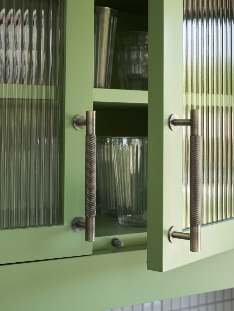 Sage green kitchen cabinet detail featuring reeded glass panels with antique brass knurled T-bar handles, showcasing Roundhouse Design's signature hardware and traditional craftsmanship with contemporary colour palette