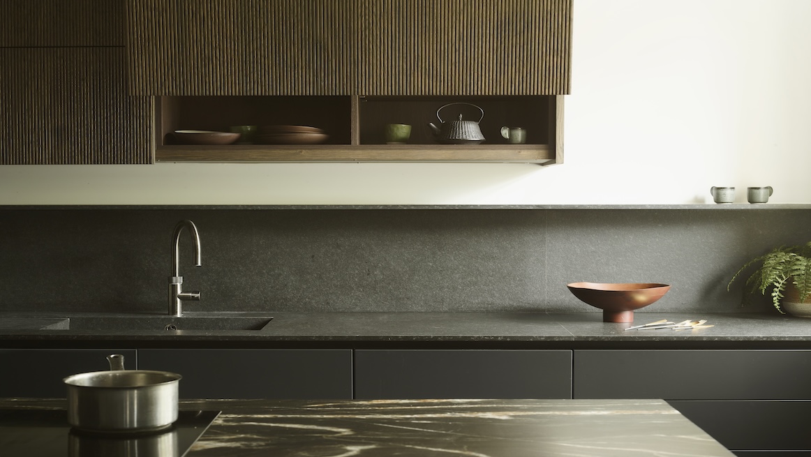 Contemporary kitchen with fluted timber wall units, charcoal grey base cabinets, honed limestone worktops and splashback, featuring chrome tap and copper accent bowl