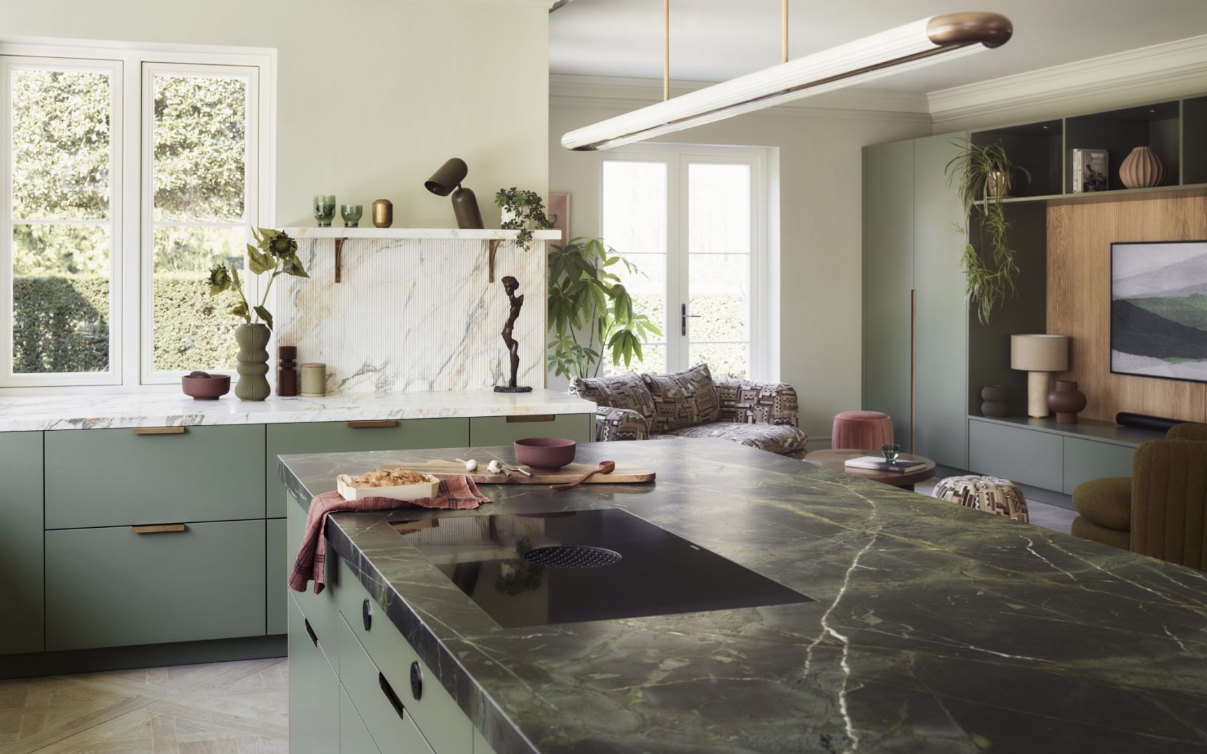 Contemporary bespoke kitchen with sage green cabinetry flowing seamlessly into an integrated living room media wall, creating a cohesive invisible kitchen design.