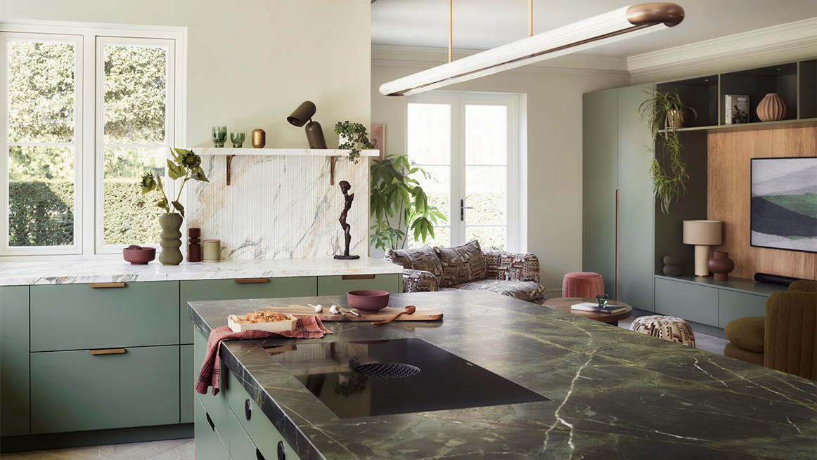 Sage green kitchen featuring dramatic veined marble worktop and splashback, brass accents, floating timber shelf, and seamless flow into living area with contemporary pendant lighting