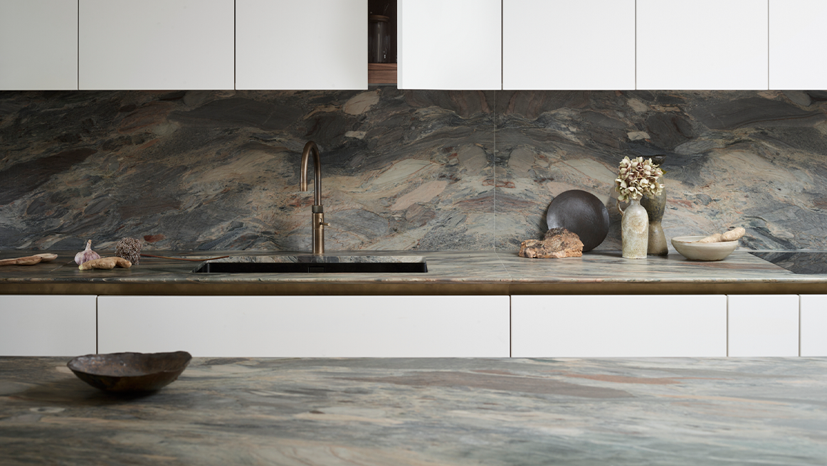 Dramatic bookmatched marble worktop and full-height splashback with bold grey veining, white handleless base cabinets, and brass mixer tap creating luxurious focal point
