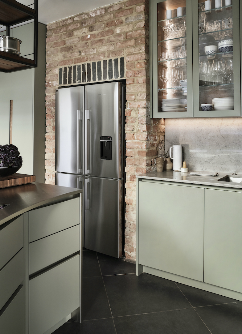 Sage green handleless kitchen with exposed brick wall, integrated American-style fridge-freezer, glazed wall units and grey marble worktop in period property