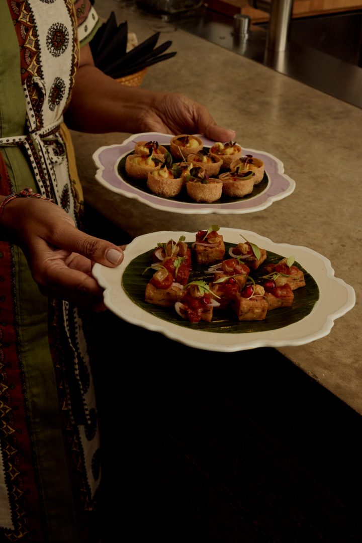 Catering staff presenting gourmet canapés on white scalloped serving plates at Roundhouse event, featuring artisan hors d'oeuvres with edible flowers and microgreens on polished concrete worktop
