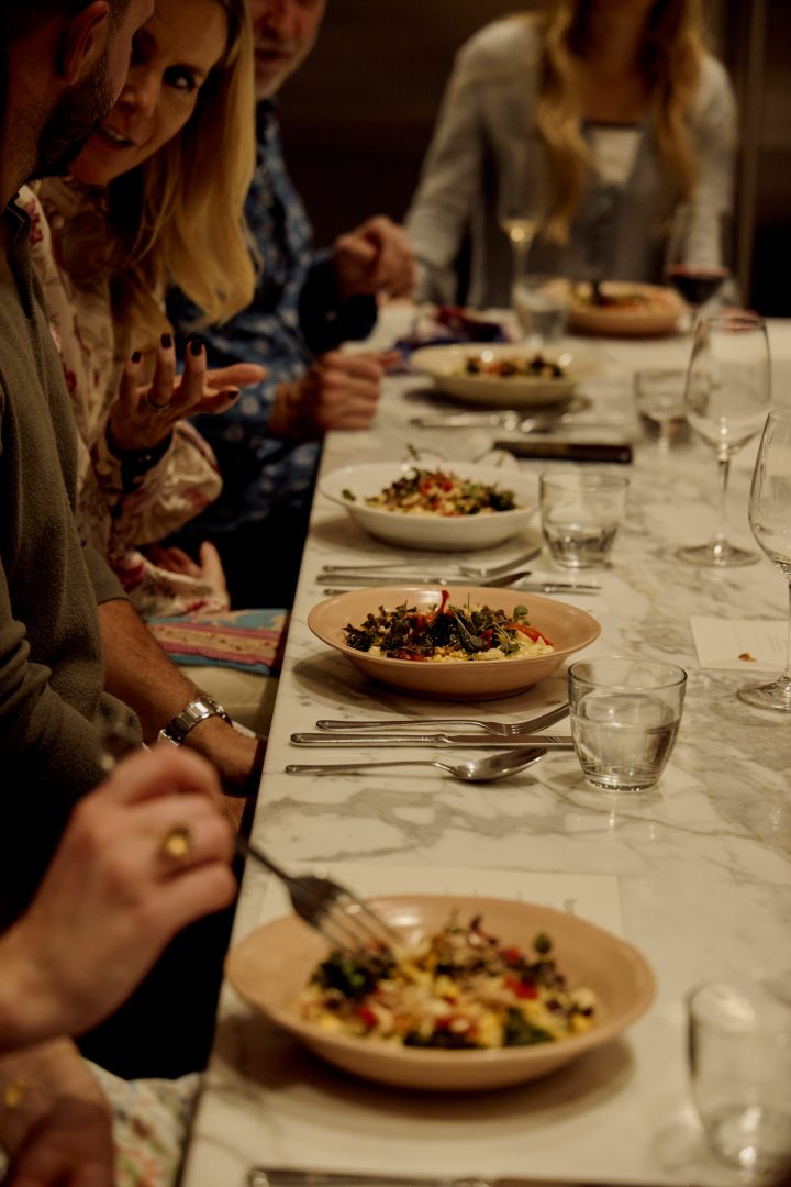 Guests dining at Roundhouse event with artisan dishes served on ceramic plates at white marble table, intimate candlelit atmosphere with engaged conversation