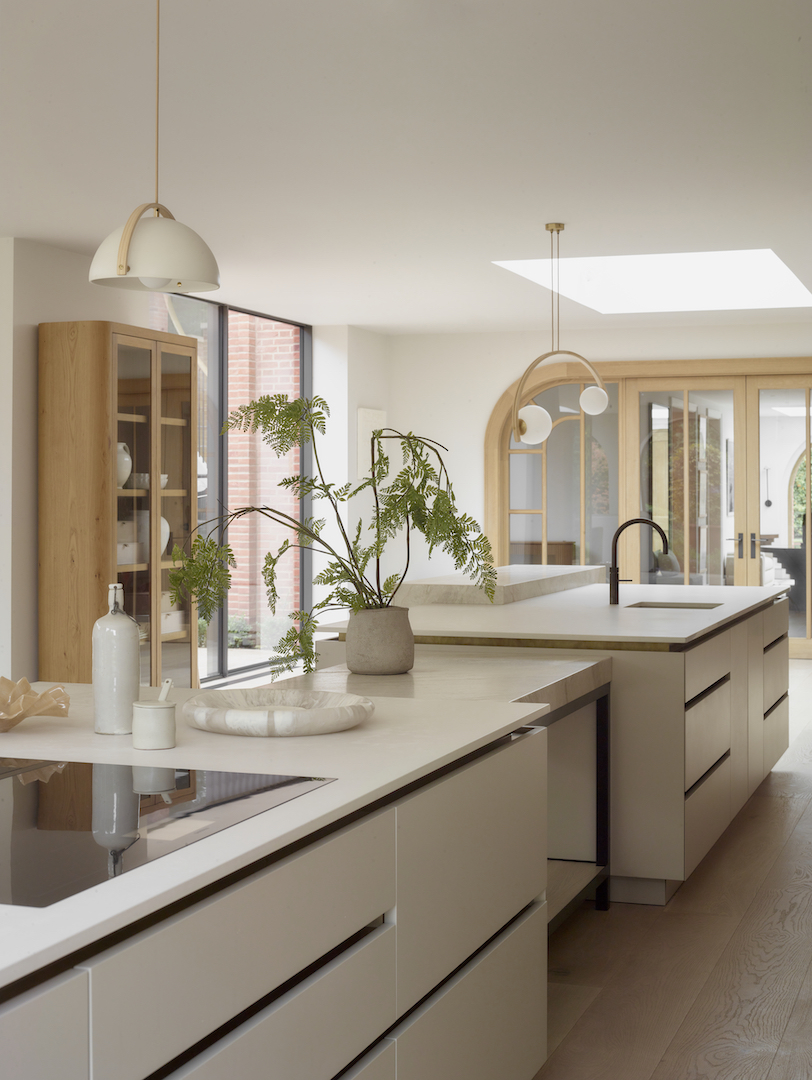 Light oak and cream handleless kitchen with arched glass doors, skylight, dual islands featuring white quartz worktops and brass pendant lighting