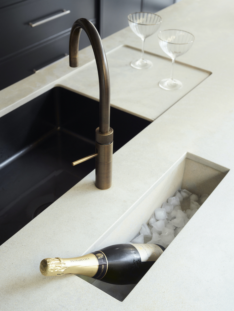 Brushed brass kitchen tap with knurled detail above integrated champagne trough in white quartz worktop with black undermounted sink