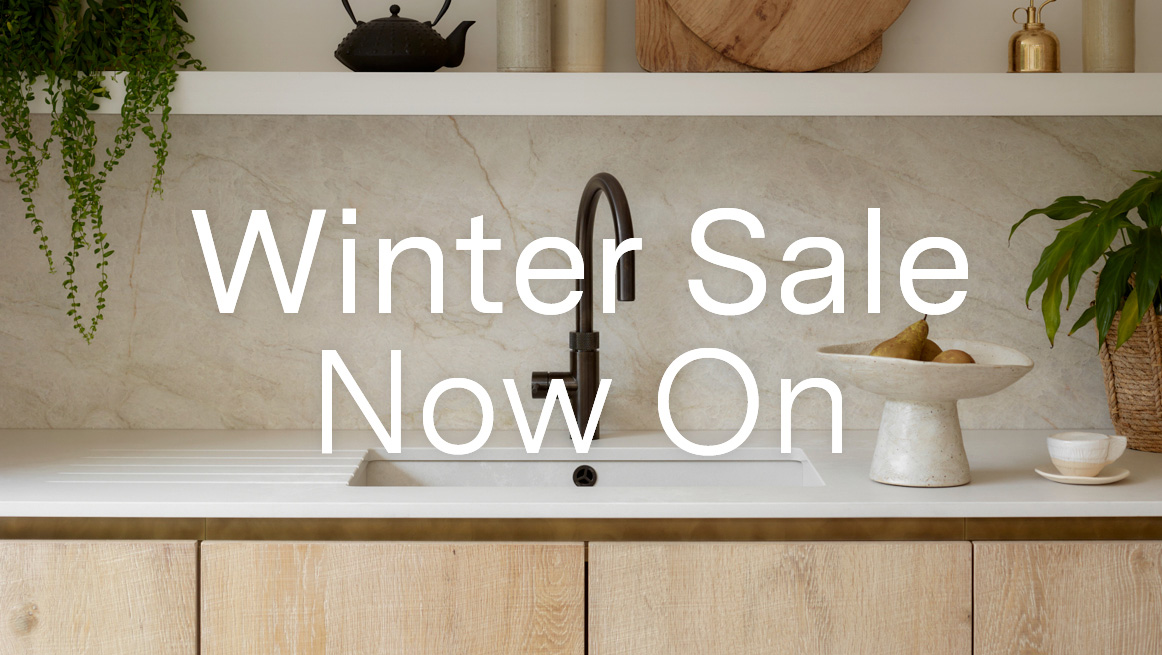 Luxury bespoke kitchen with pale oak cabinetry and marble worktop displaying Winter Sale Now On promotional text, featuring black designer tap and curated styling