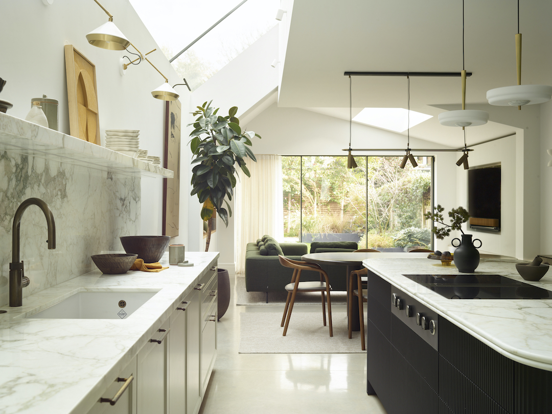 Open-plan kitchen extension with Carrara marble worktops, fluted island cabinetry, skylight glazing and brushed brass pendant lighting overlooking garden