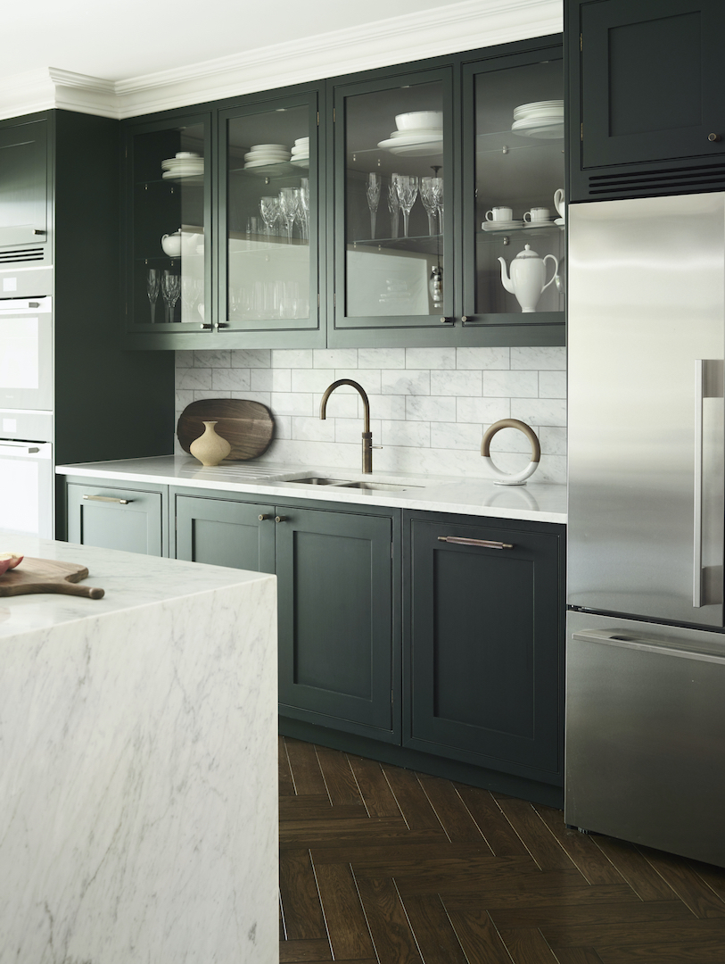 Deep forest green Shaker kitchen with glazed display cabinetry, white marble metro tile splashback, bronze tap and white Carrara marble waterfall island