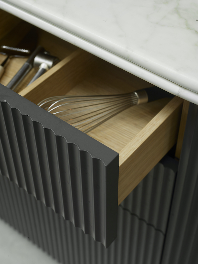 Open drawer revealing solid oak interior with bespoke cutlery divider and white marble worktop above charcoal fluted cabinetry facade