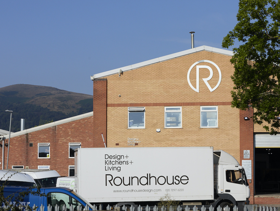 Roundhouse Design manufacturing facility exterior with branded delivery vehicle reading Design + Kitchens + Living, showcasing British craftsmanship headquarters with mountain backdrop