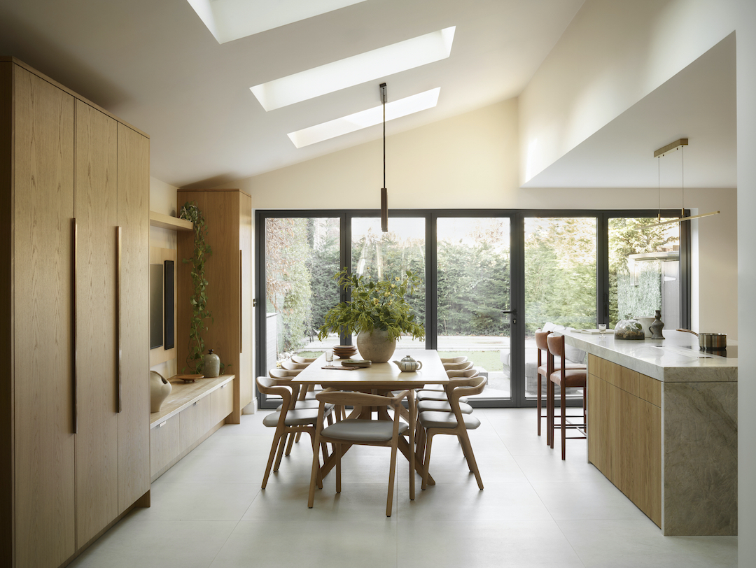 Open-plan kitchen dining extension with natural oak cabinetry, skylights, slate-framed doors to garden, and integrated breakfast bar with marble waterfall edge