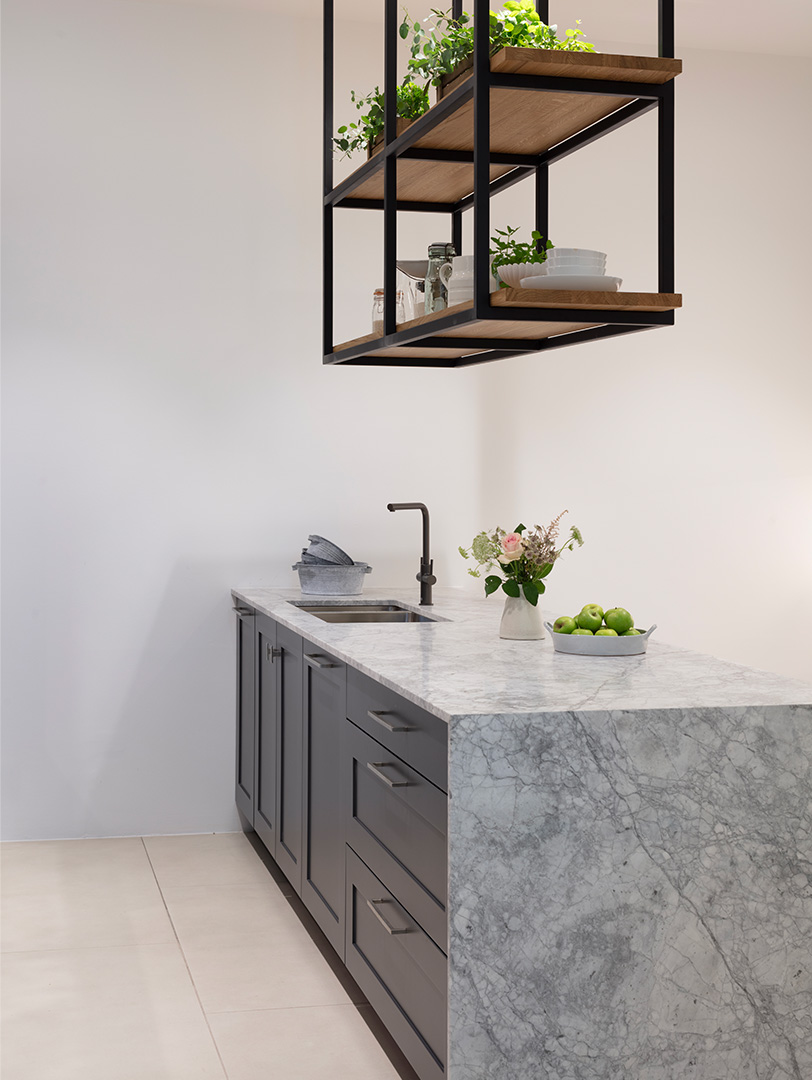 Charcoal grey Shaker kitchen island with book-matched marble waterfall worktop, black tap and suspended oak shelving with steel frame displaying fresh herbs