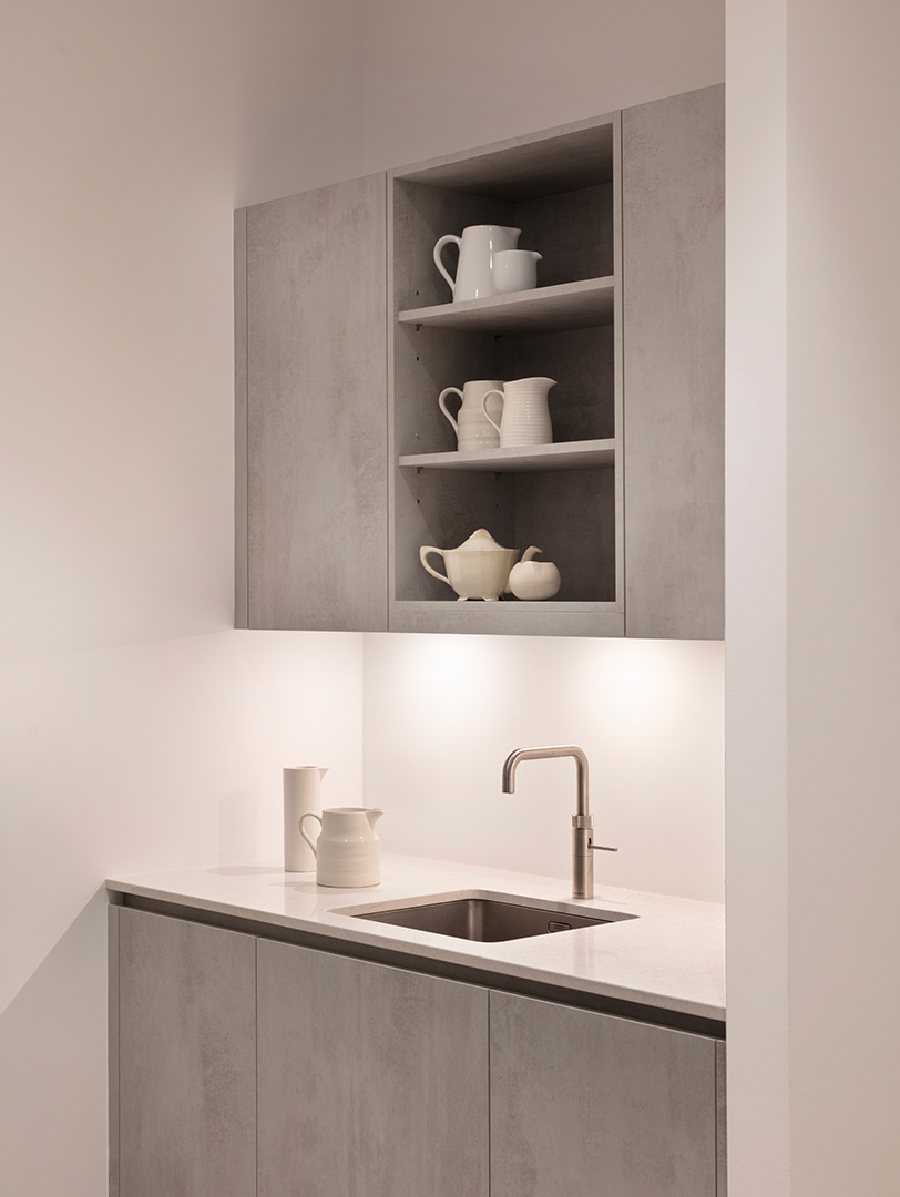 Minimalist concrete-effect handleless kitchen cabinetry with open display shelving, white quartz worktop and brushed nickel tap over undermount sink