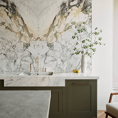 Bespoke kitchen featuring book-matched marble splashback with brass tap and sage green Shaker cabinetry with marble worktop
