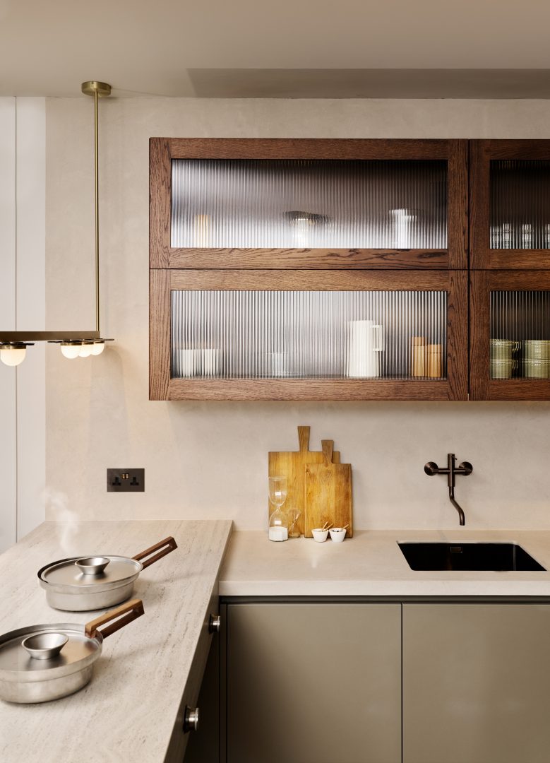 Bespoke kitchen display featuring warm neutral cabinetry, ribbed glass wall units, stone worktops, a black integrated sink and tap, and contemporary brass lighting at the Roundhouse + Day True Wimbledon showroom.