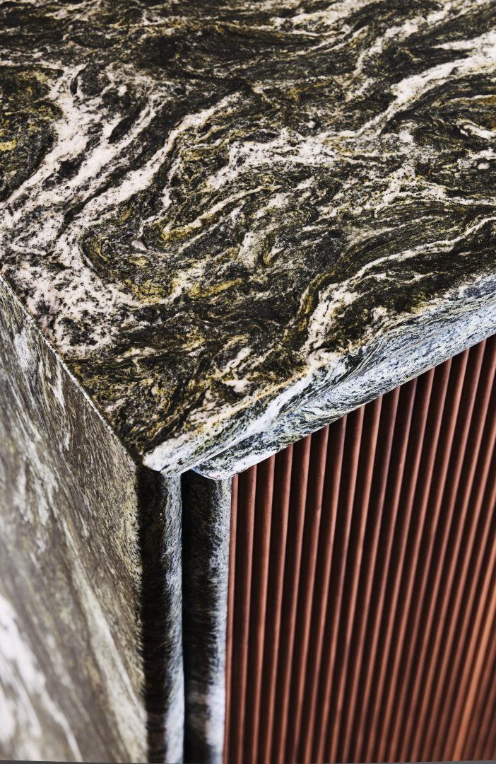 Detail of a Calacatta marble bathroom worktop with integrated basin, black wall-mounted tapware and bespoke fluted walnut cabinetry at the Roundhouse + Day True Wimbledon showroom.