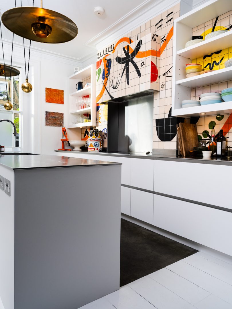 A contemporary white bespoke kitchen with stainless steel worktops, open shelving and a hand-painted abstract tiled splashback, designed for Yotam Ottolenghi by Roundhouse.