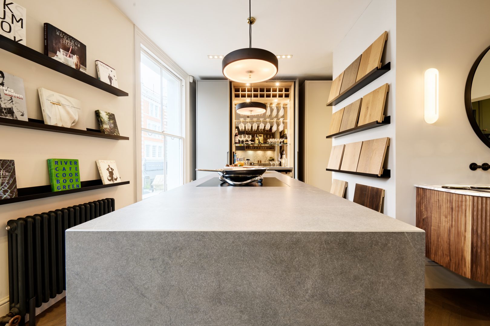 Roundhouse + Day True showroom display showcasing a floating fluted walnut bathroom vanity with marble worktop, circular mirror, contemporary wall lighting and a bespoke kitchen display beyond.
