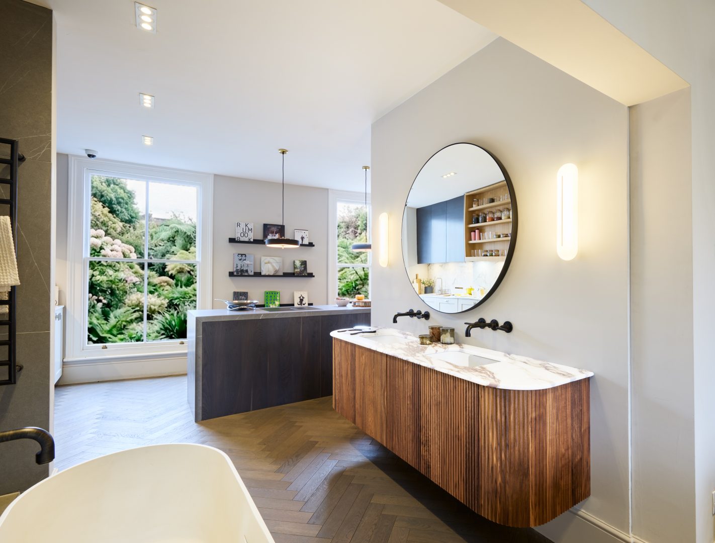 Bespoke Roundhouse kitchen display featuring a large stone-clad island with integrated induction, open shelving, timber finish samples and a glazed drinks cabinet at the Roundhouse + Day True Wimbledon showroom.