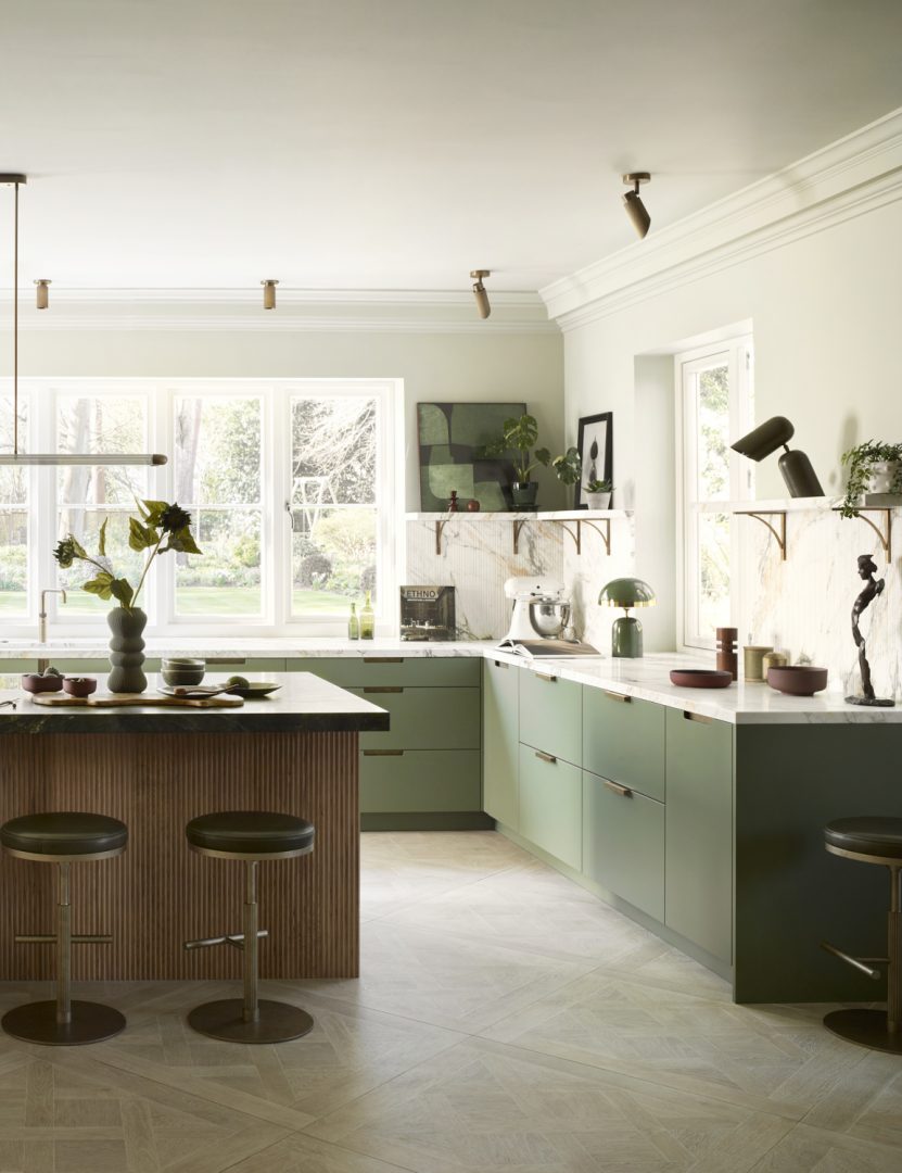 Bespoke green kitchen with pistachio green painted cabinetry, fluted oak island, marble worktops, brass details and garden views.