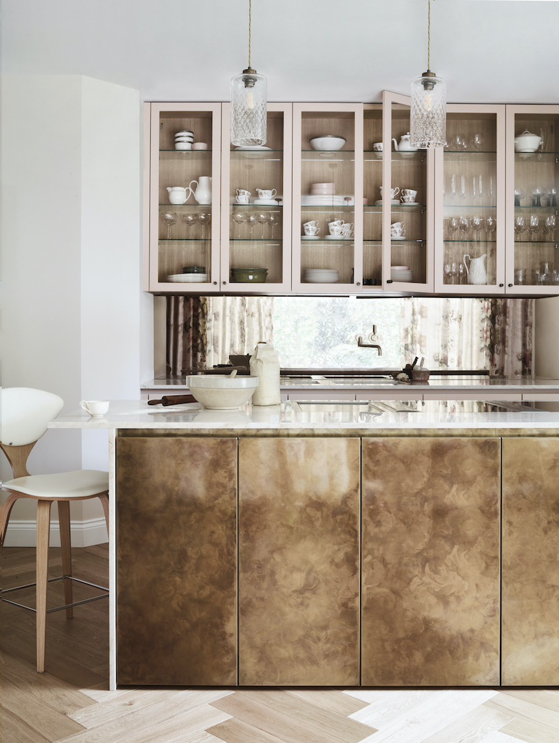Luxury kitchen with glazed display cabinetry, statement brass island, marble worktop and metallic splashback.