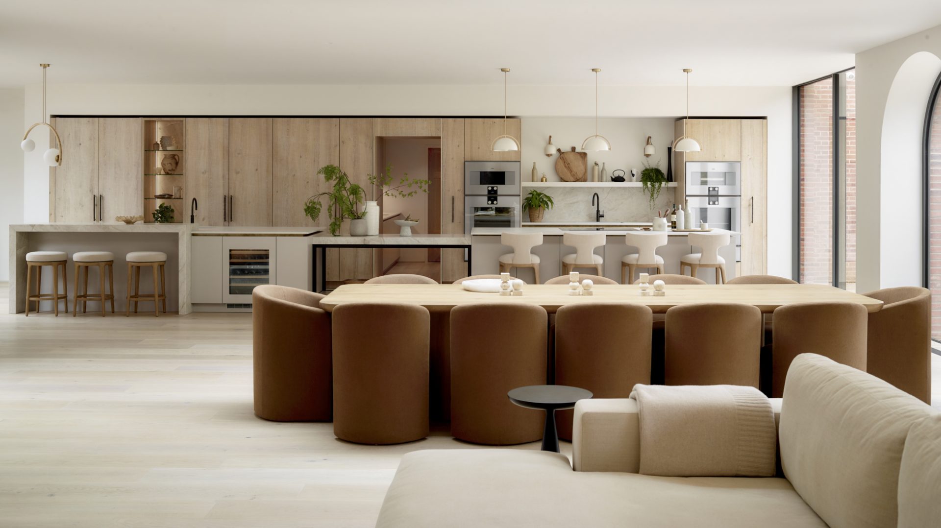 Bespoke open-plan kitchen with natural oak cabinetry, stone worktops, dining space and sofa area showcasing soft kitchens, timeless kitchen design and natural materials for modern family living.