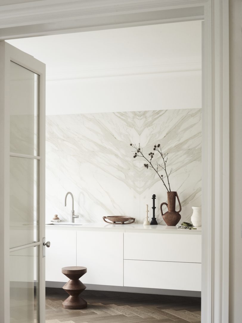 Minimal white kitchen cabinetry with bookmatched marble splashback, timber flooring and contemporary slab doors.