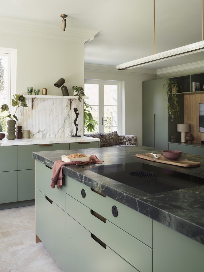 Bespoke green kitchen with contemporary cabinetry, natural stone island, fluted stone splashback and open-plan living area.