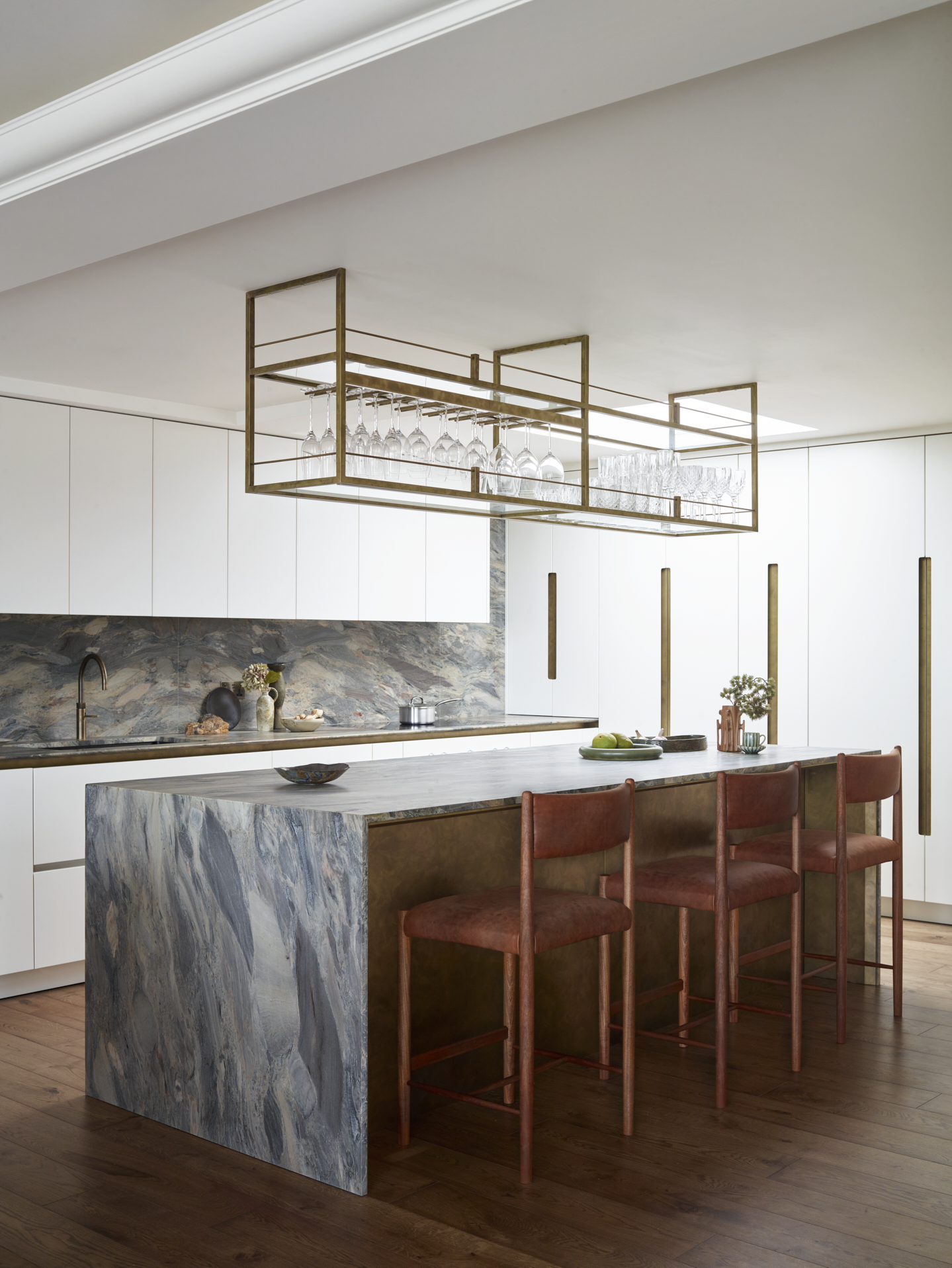 Minimal white kitchen design showcasing statement quartzite stone waterfall worktops and splashback. Featuring antique brass wrapped cabinetry and detailing.