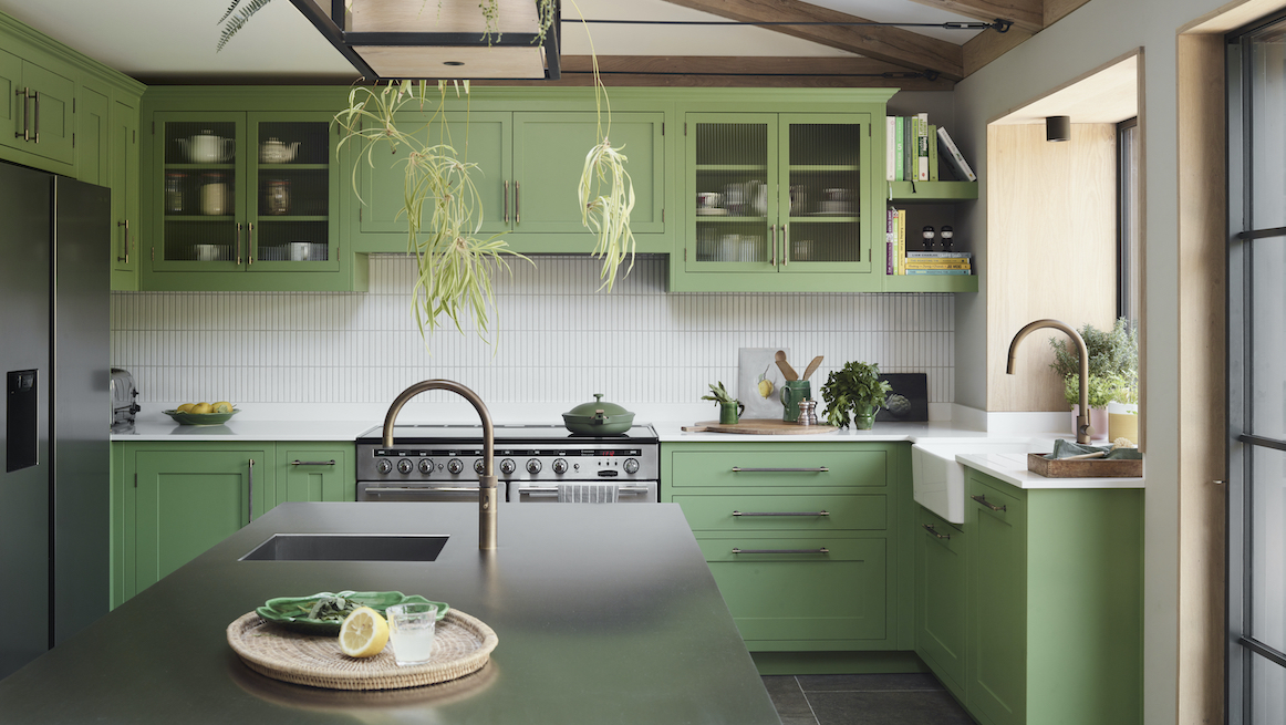 Bespoke Oliver kitchen with Botanical Green cabinetry, white Kit Kat tiles, oak accents and stainless-steel worktops, creating a fresh, light-filled scheme.