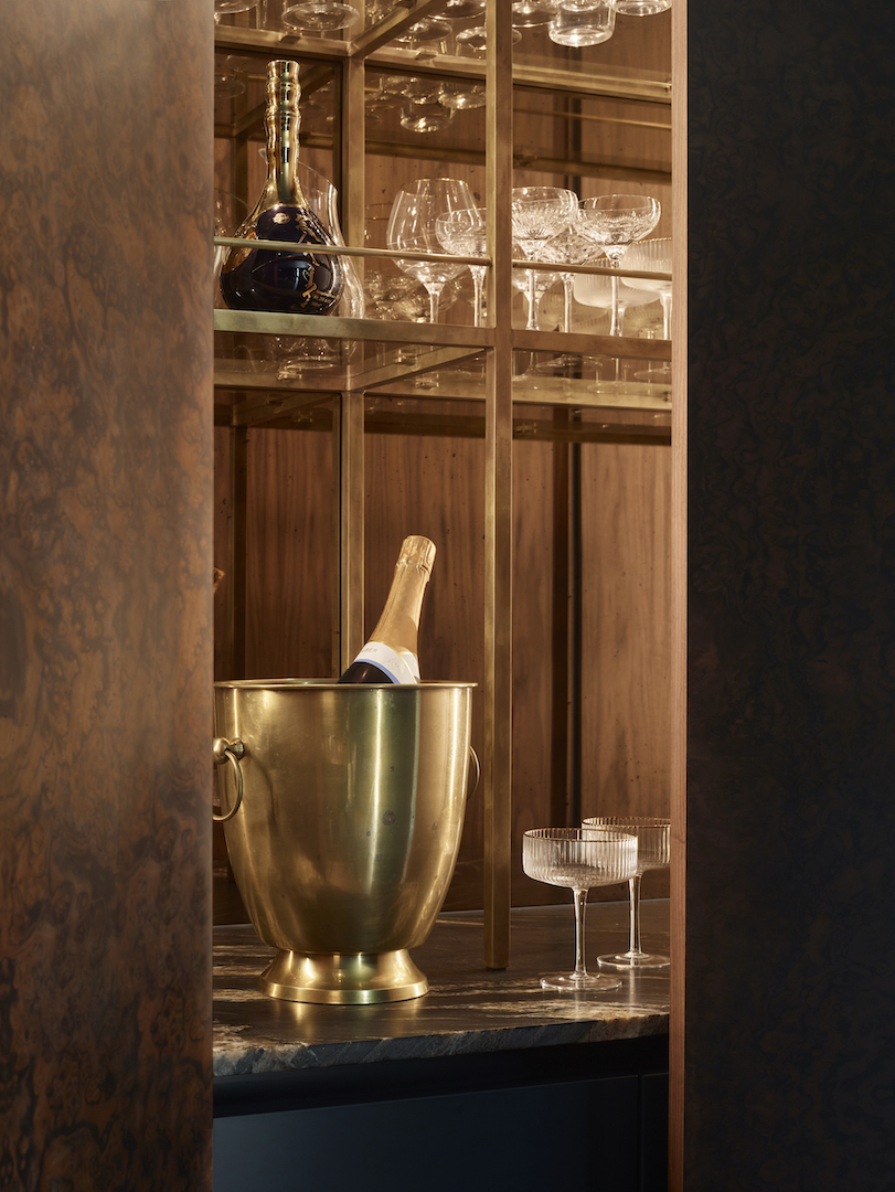 Bespoke home bar with glass storage, warm timber interiors and metallic cabinetry by Roundhouse