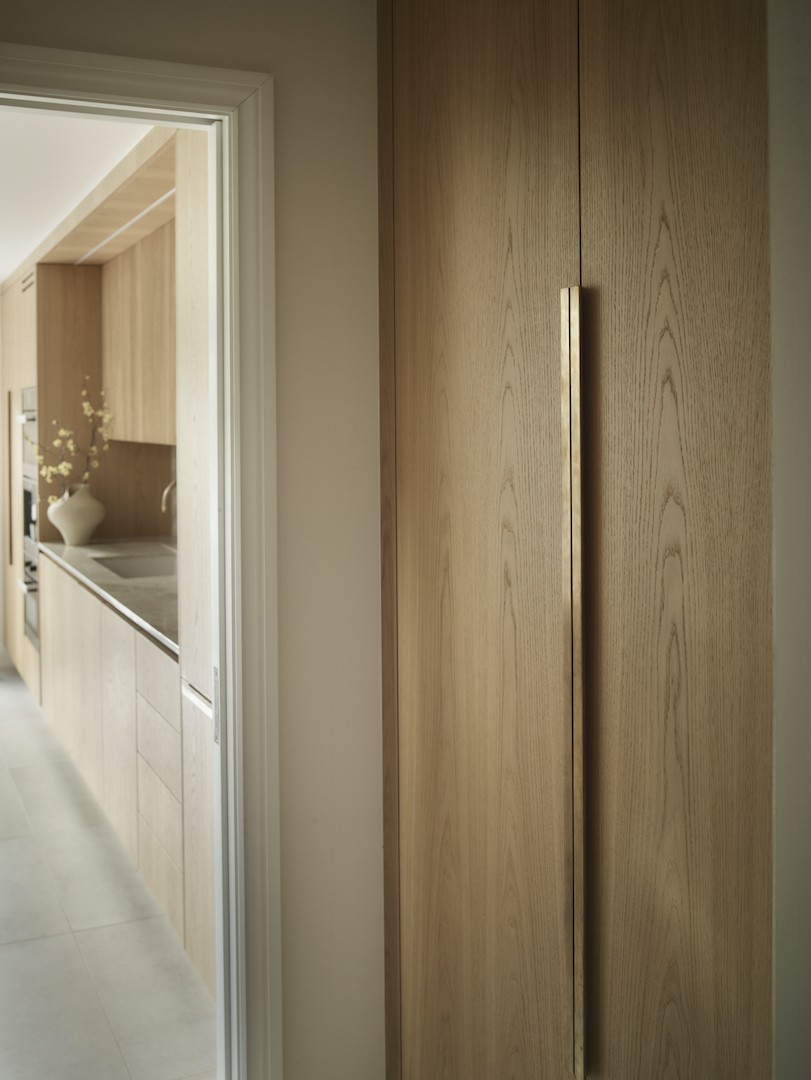 Floor-to-ceiling bespoke oak cabinetry with long brass handle beside a contemporary Roundhouse kitchen