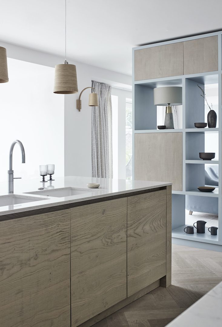 Pale blue and rough-sawn oak bespoke kitchen with textured timber island and open shelving.