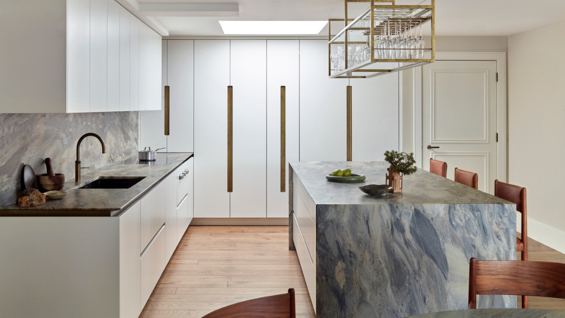 Bespoke luxury kitchen with handleless white cabinetry with integrated brass pulls, concealed storage and a statement stone waterfall island designed for a seamless contemporary interior.