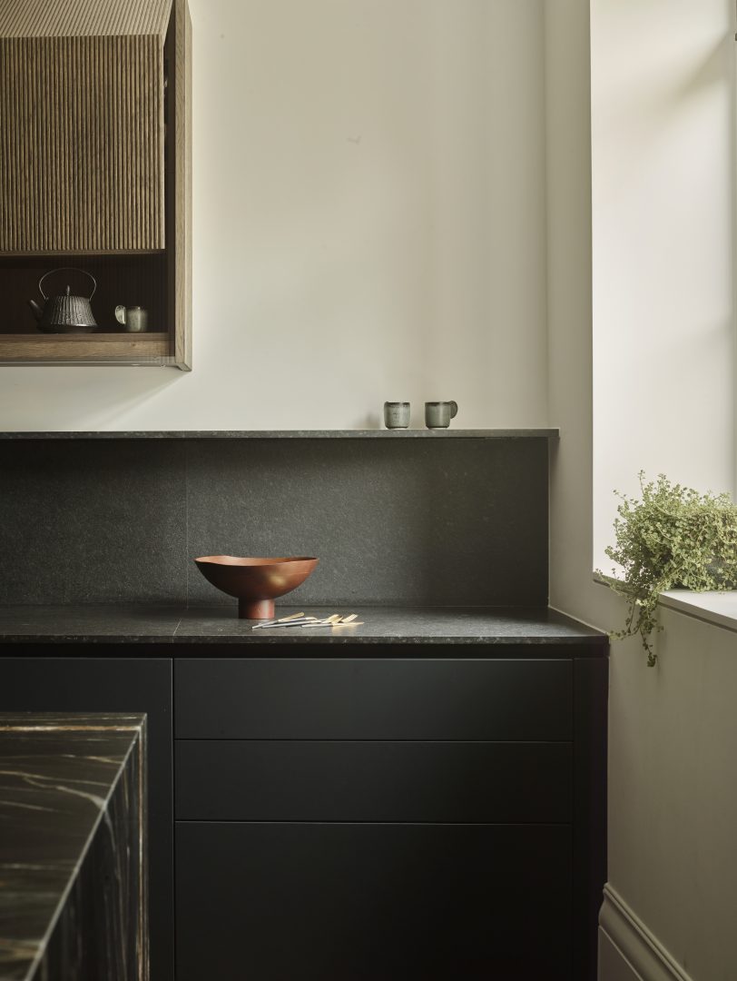 Dark bespoke kitchen with a black granite worktop, matching splashback and timber breakfast bar