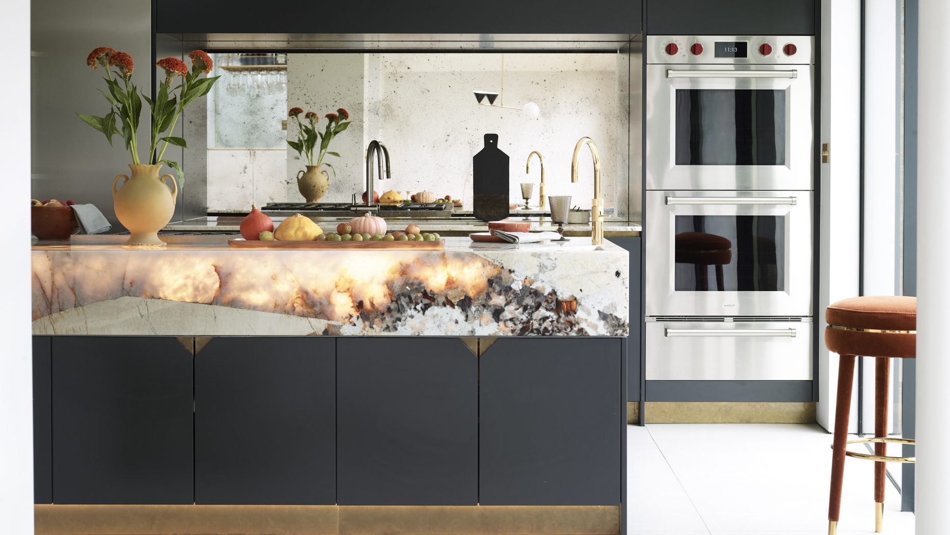 Bespoke dark kitchen with a dramatic backlit natural stone island worktop and mirrored splashback