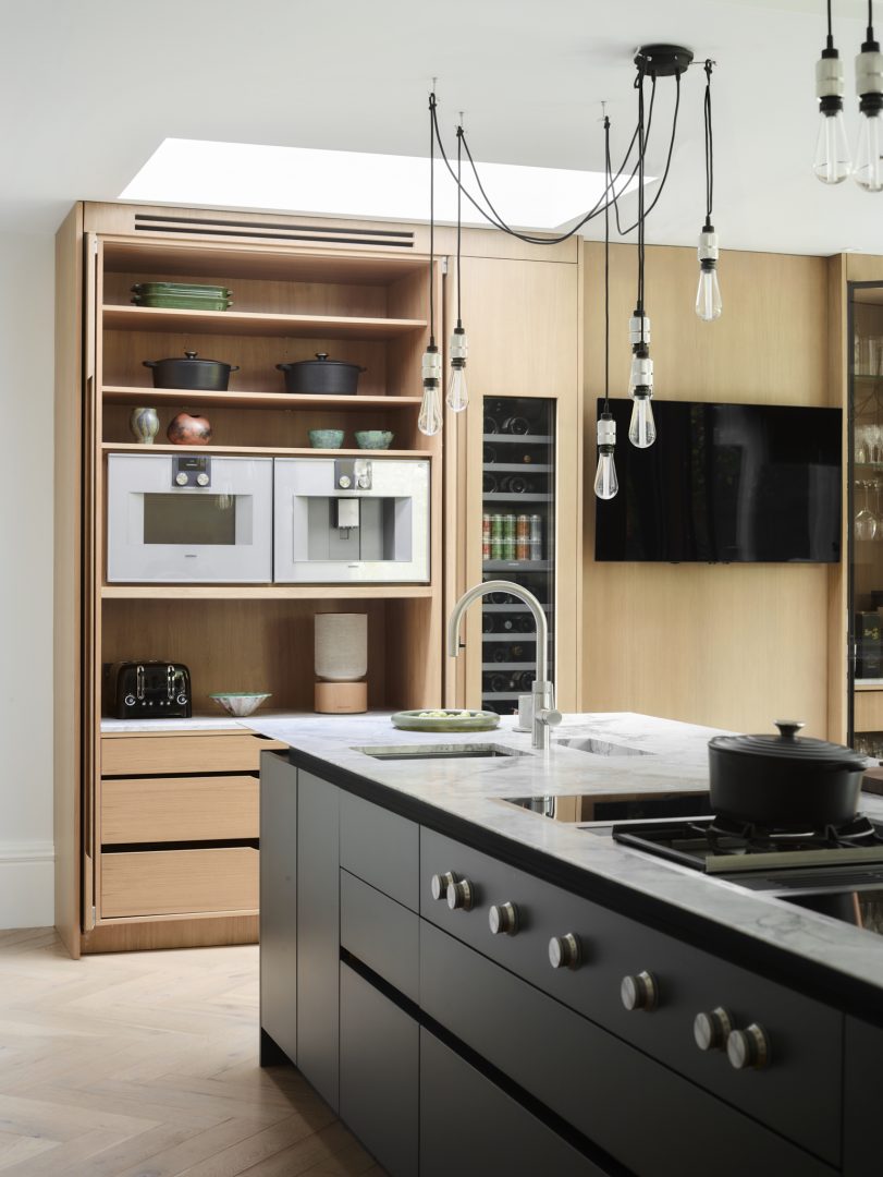 Pocket doors opening to reveal concealed kitchen appliances and storage within a bespoke oak pantry, creating a clean, clutter-free kitchen.