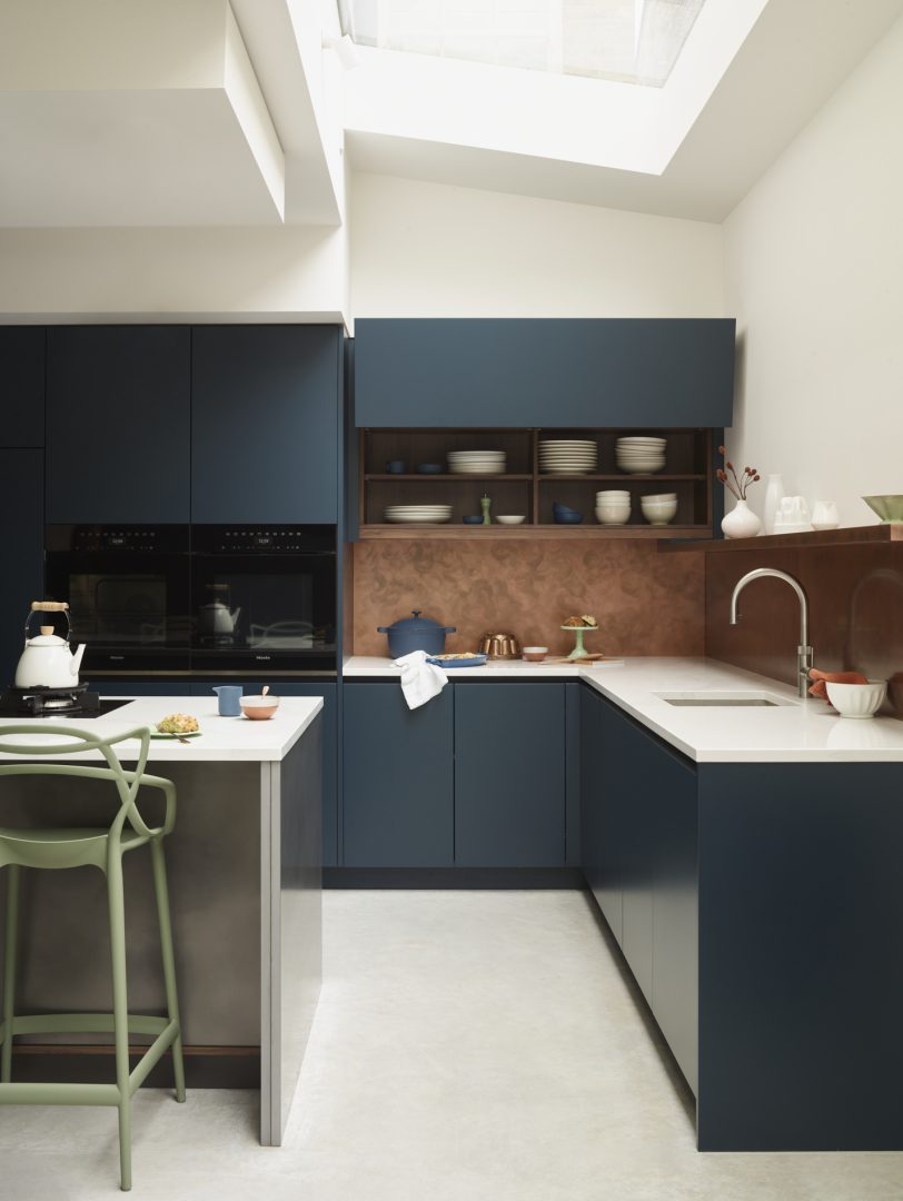 Contemporary navy blue kitchen with a light worktops, stainless steel island and copper splashback