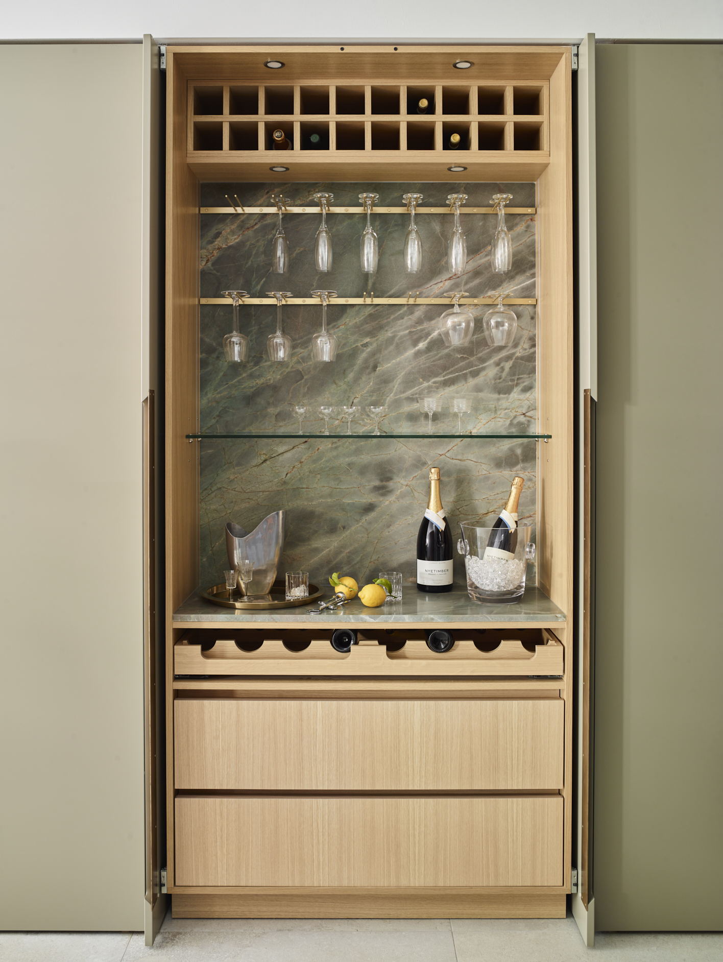 Concealed luxury home bar with natural oak bespoke cabinetry, integrated wine storage and green stone splashback, hidden behind complementary green pocket doors.