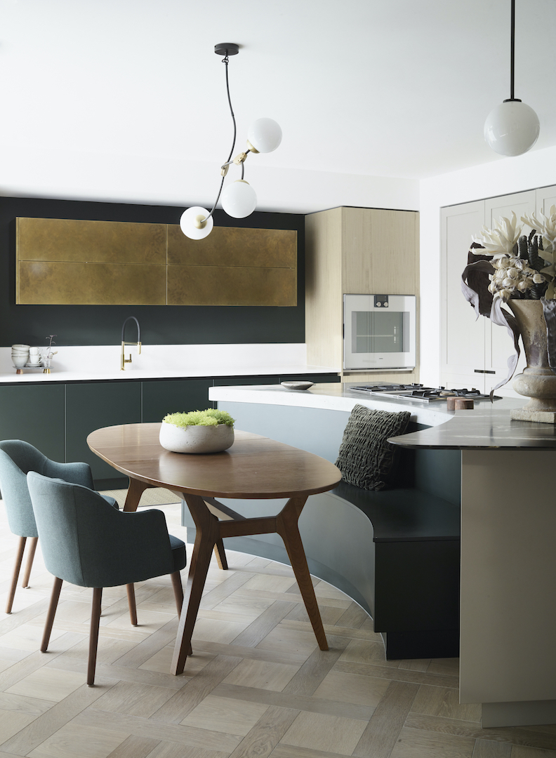 Curved bespoke kitchen island wrapping around an oval dining table and banquette seating in a light-filled open-plan kitchen.